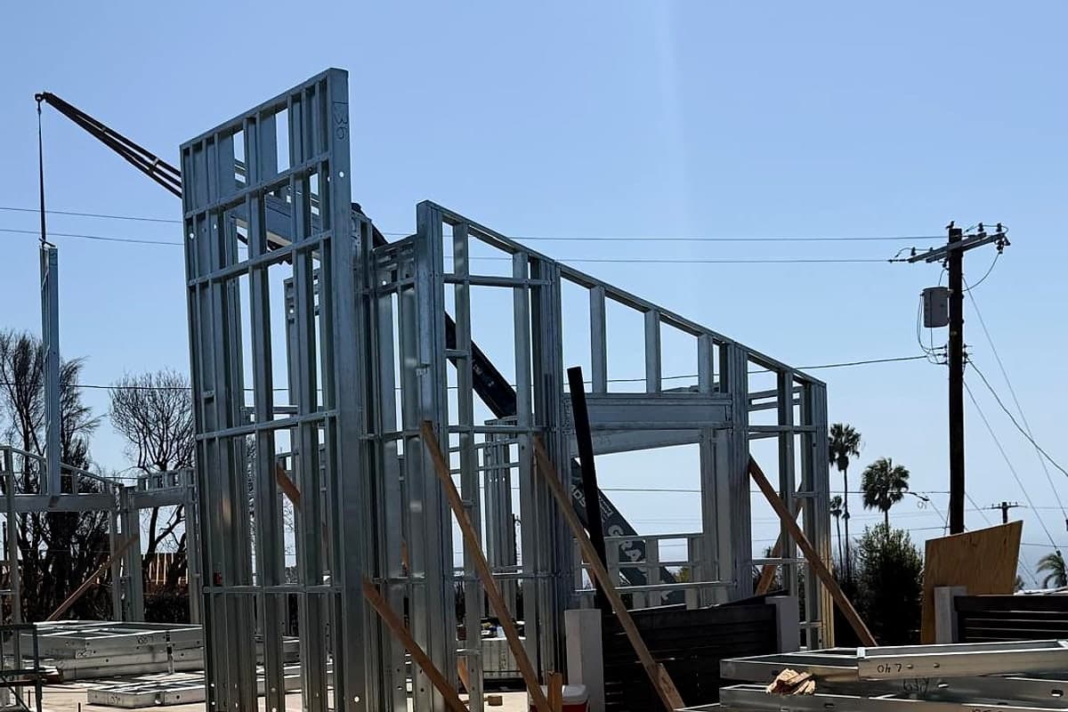 A tall steel wall panel standing beside the crane that set it, on a Pacific Palisades rebuild