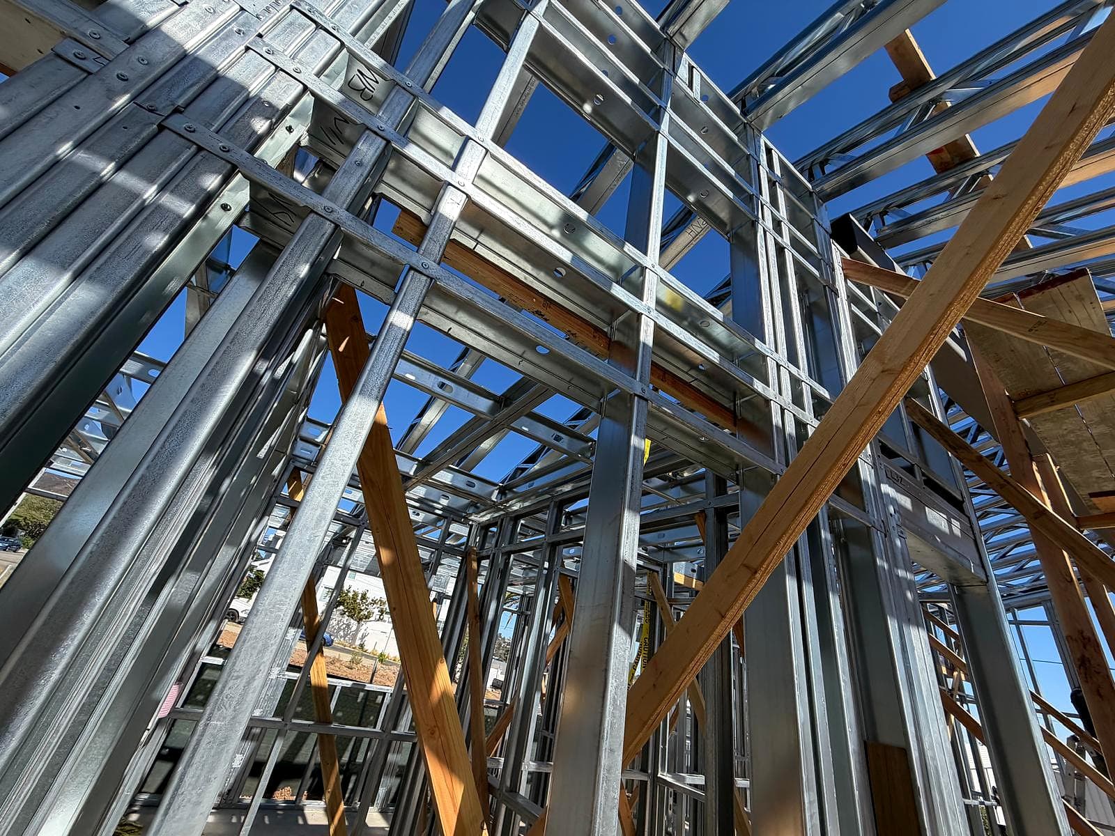 Looking up through layered galvanized steel studs, headers and straps with screws visible at each connection
