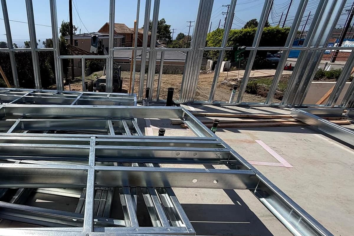 A prefabricated steel wall panel lying on the slab, its studs and tracks forming a grid