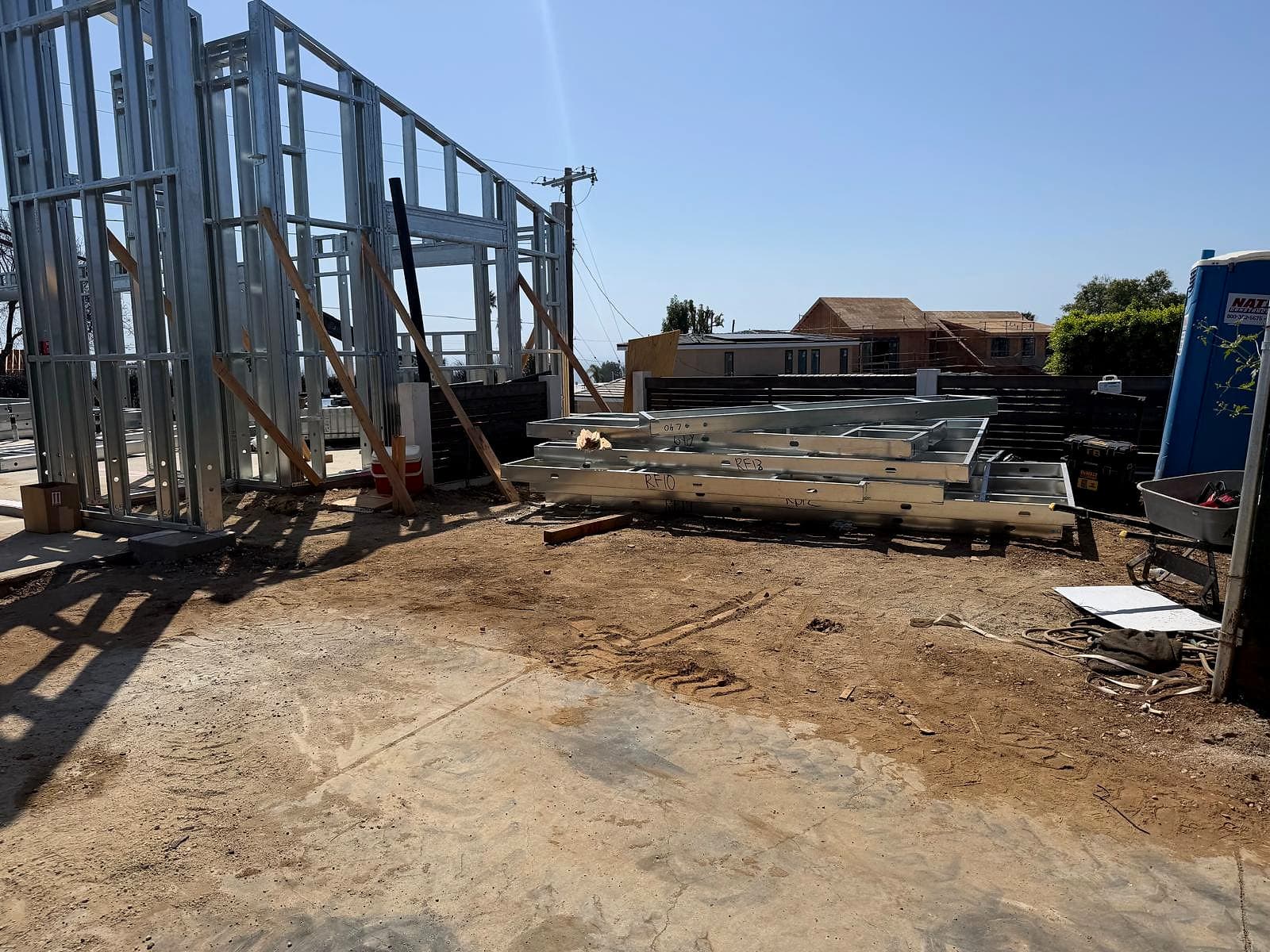 Stack of prefabricated galvanized steel wall panels marked RF10 and RF13 lying beside braced steel walls