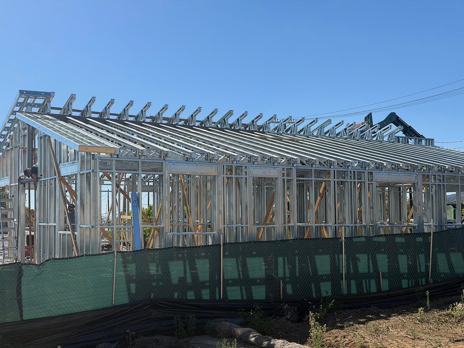 Side view of the whole house in light-gauge steel with the roof framing complete from end to end, steel rafters and outlookers against a blue sky