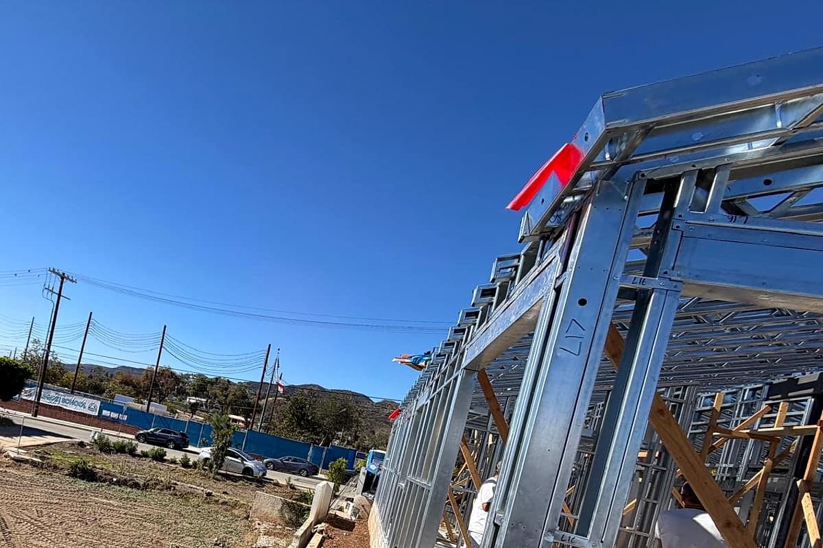 A light-gauge steel wall rising beside an open lot under a clear sky