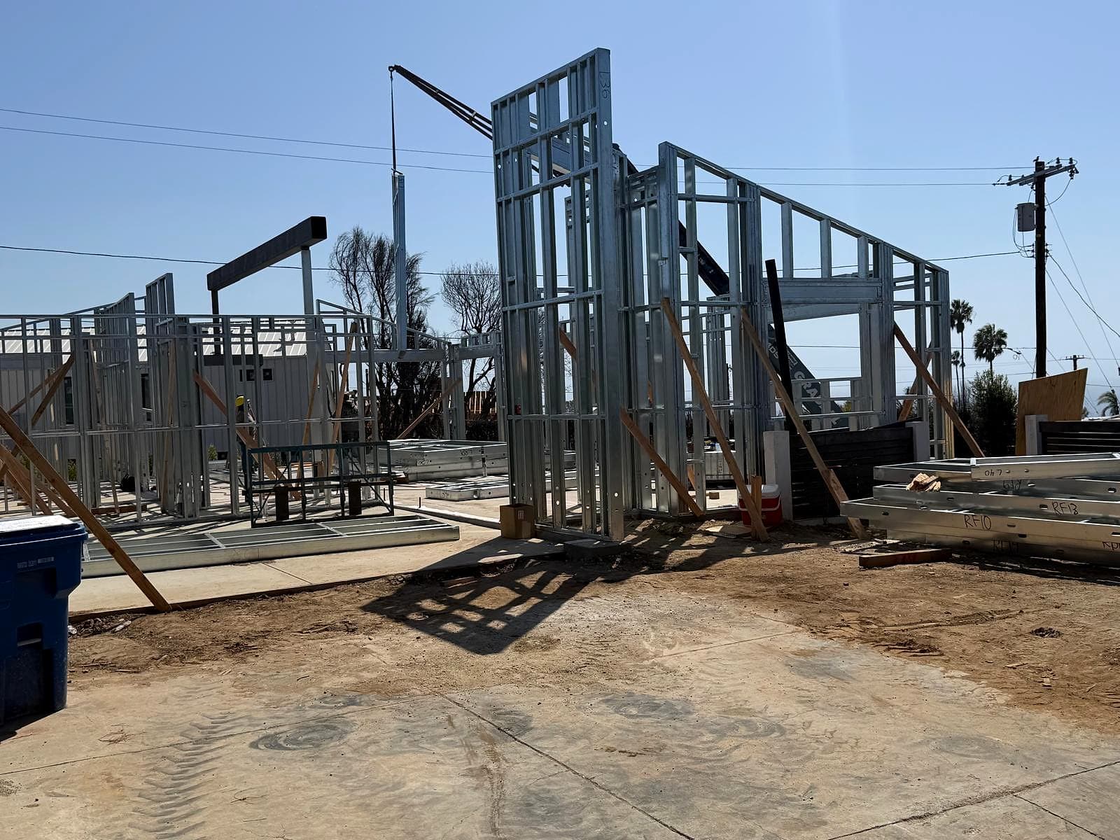 Job site in Pacific Palisades with galvanized steel wall panels standing on a slab, a crane boom behind them and numbered panels stacked on the right
