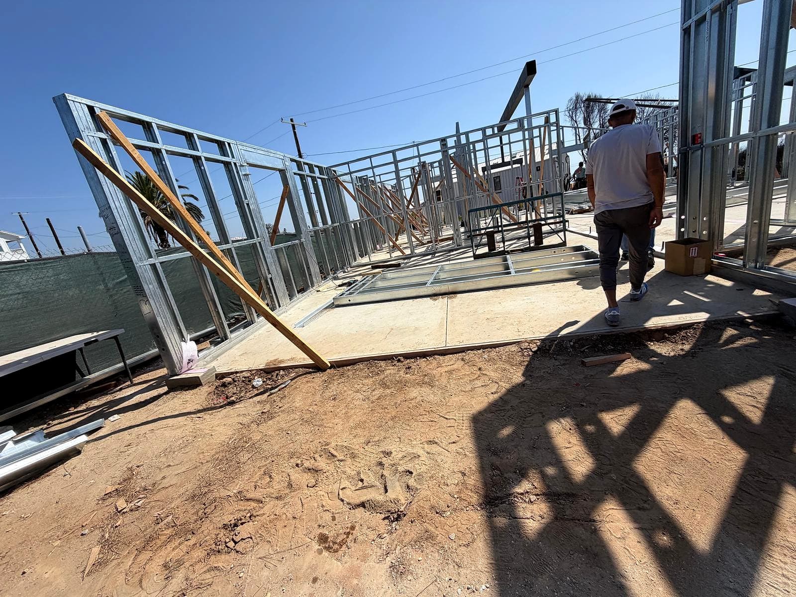 A long line of steel-framed exterior walls on a concrete slab, held plumb by diagonal wood braces